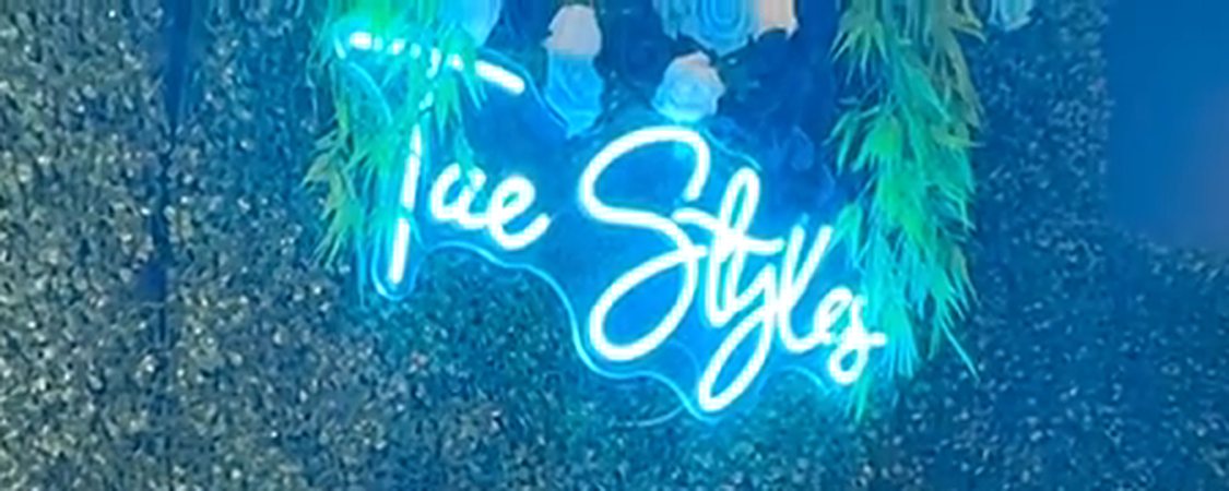 The blue Tae Styles neon sign on a greenery wall